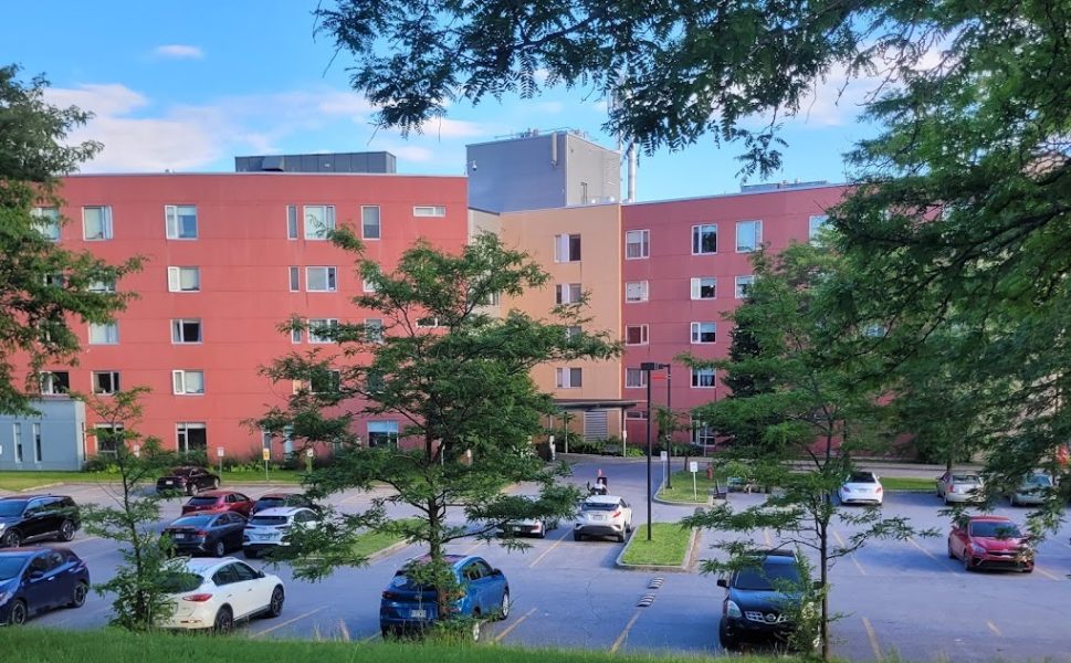 Résidence de la Cité-de-la-Santé à Laval avec façade rouge et stationnement entouré d’arbres